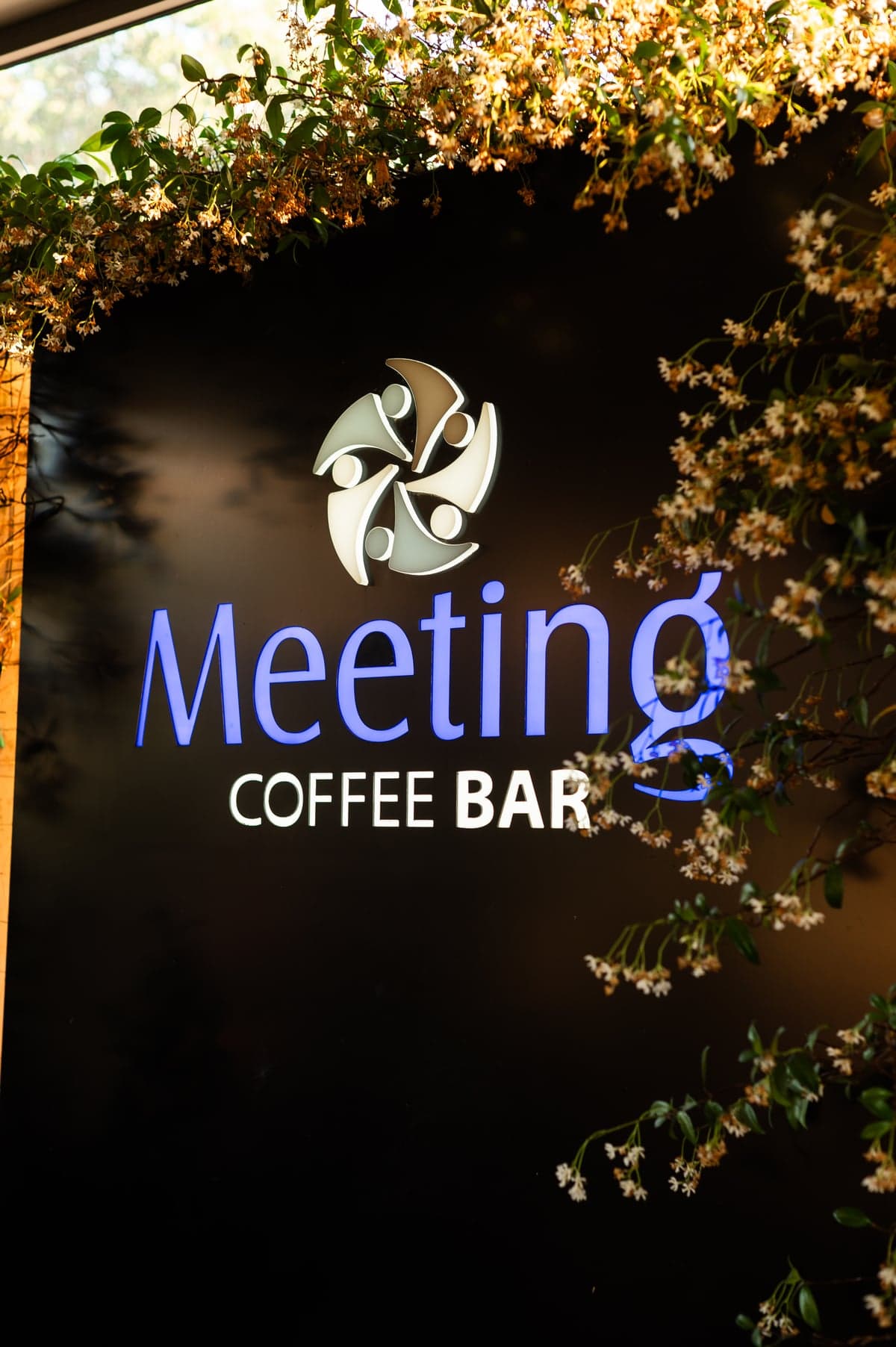 Meeting Coffee Bar — insegna illuminata tra rampicanti in fiore